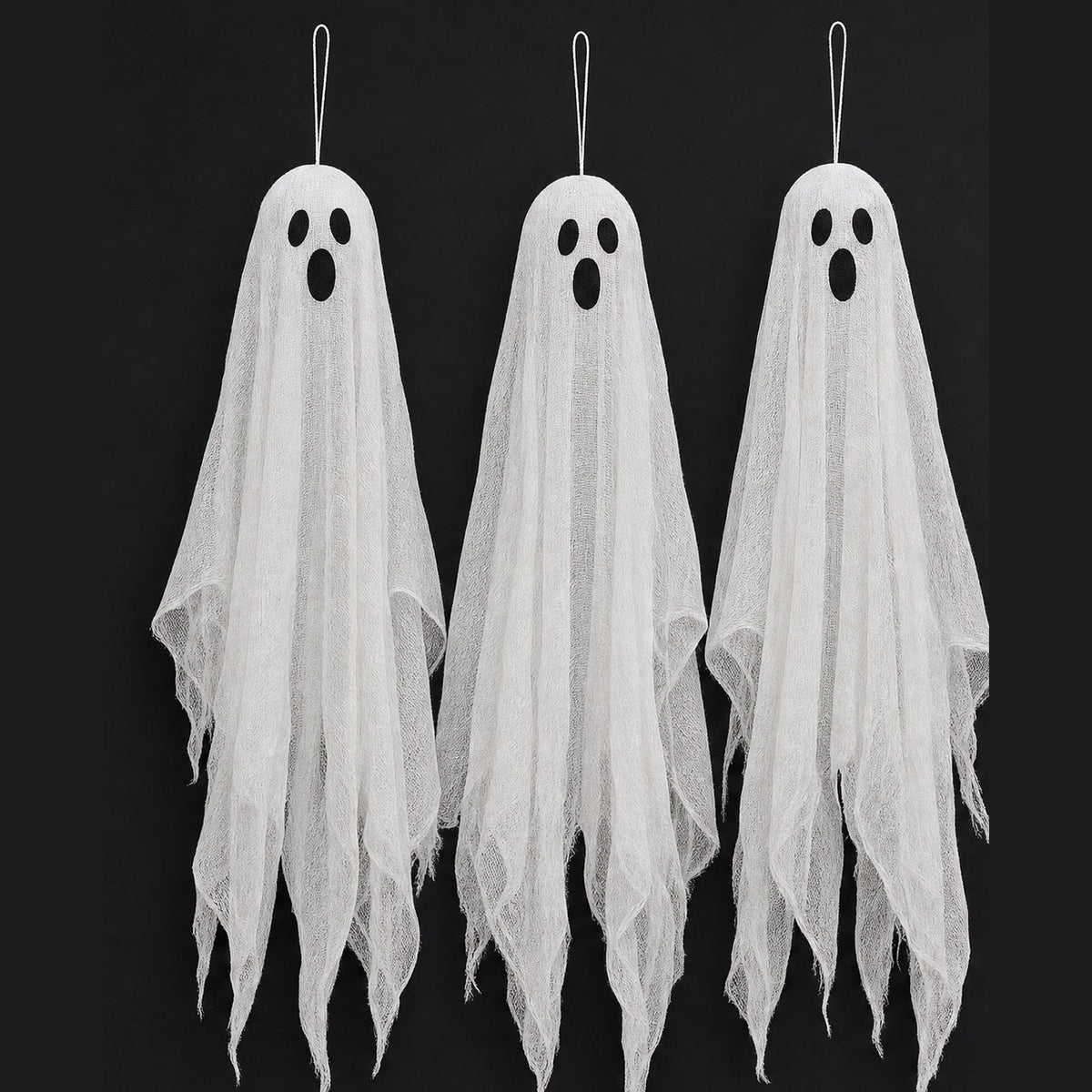Three hanging gauze ghosts with dark oval eyes against a black background