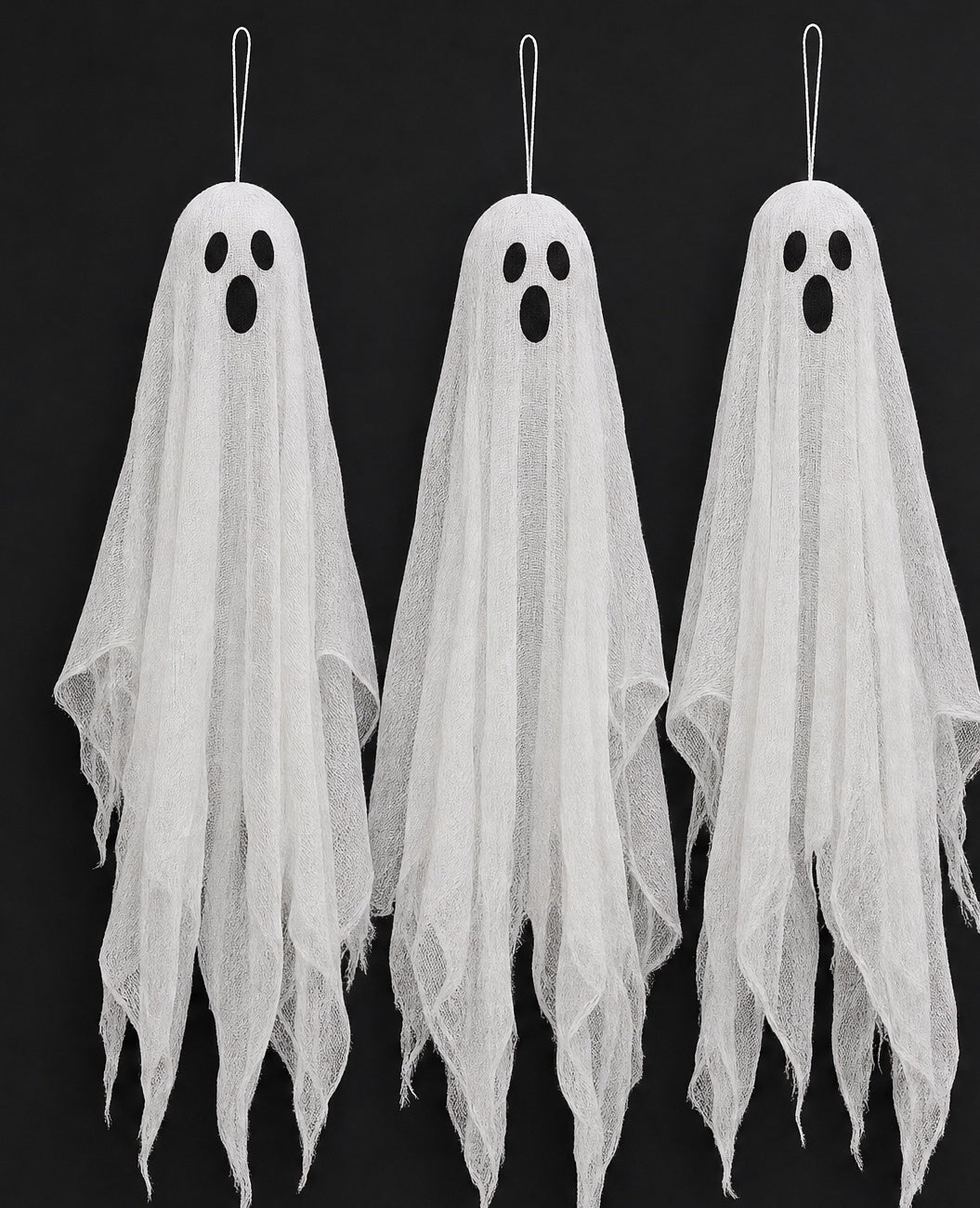 Three hanging gauze ghosts with dark oval eyes against a black background