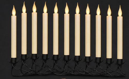Row of ivory flameless taper candles with warm flickering LED flames on a black wire garland