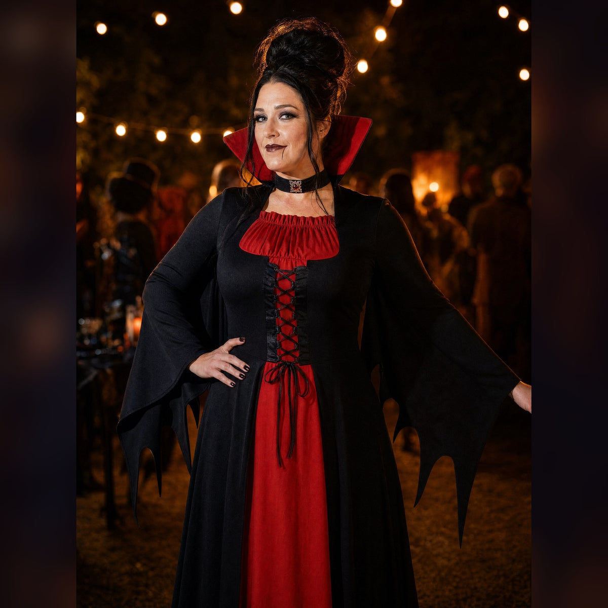 The Wraith Queen gown worn at an outdoor Halloween party at dusk, red stand-up collar and corset lacing lit by string lights