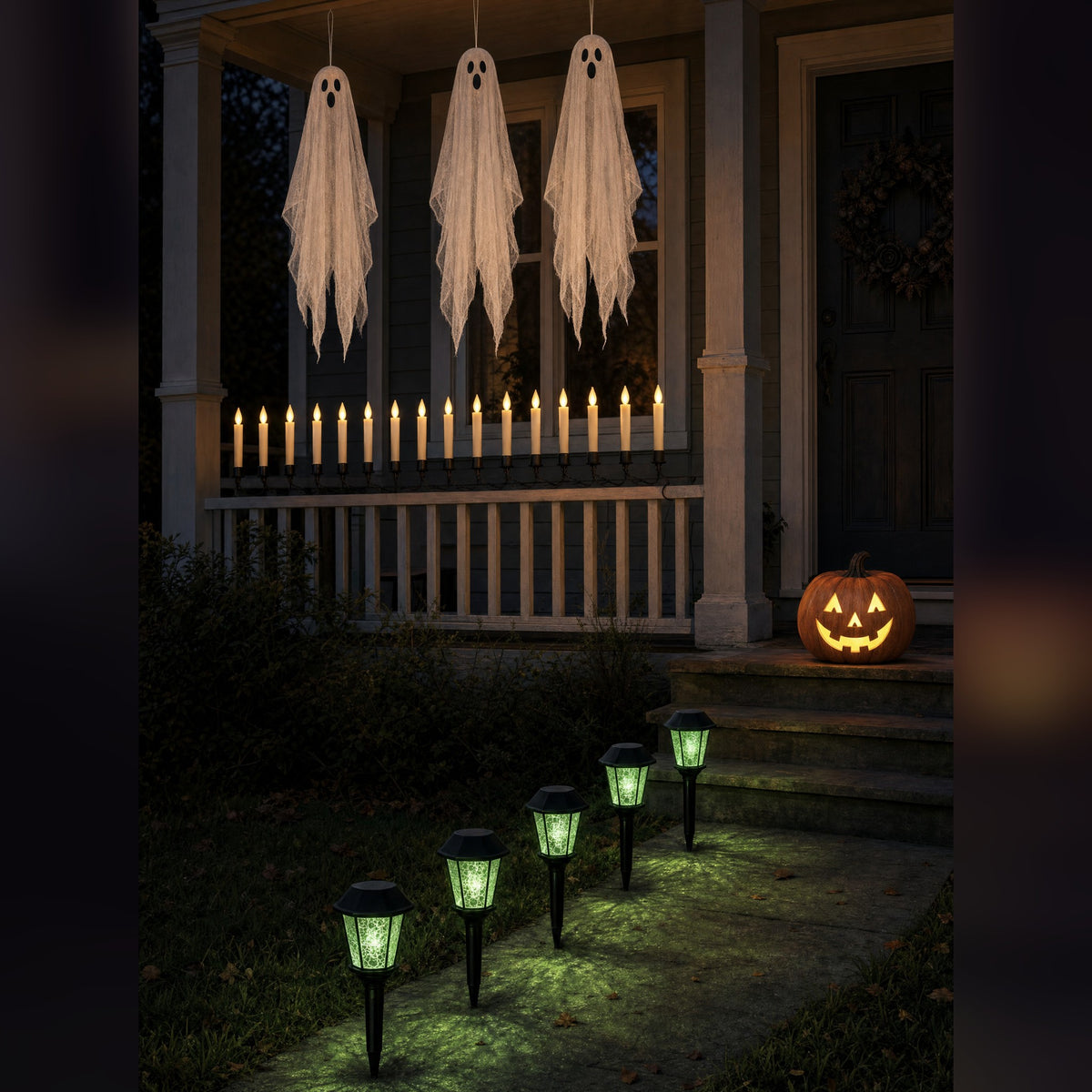 Witchlight Porch installed at dusk: three hanging ghosts, a flameless candle garland on the railing, a lit jack-o'-lantern and five green glowing lantern stakes leading up the path